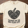 100-Year Life strength training t-shirt featuring heart-shaped weight plates and barbell design – Ivory