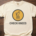Check Knees strength training t-shirt with figure holding knee in circular badge design – Ivory