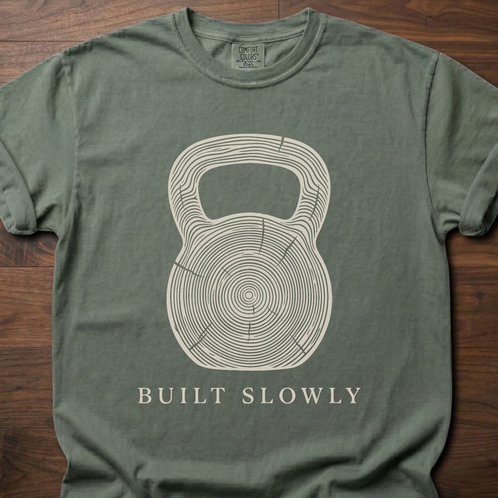 Built Slowly fitness lifestyle t shirt featuring kettlebell with tree ring growth pattern design – Moss