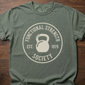 Functional Strength Society gym lifestyle shirt featuring kettlebell logo and established 1979 badge – Moss