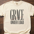 Grace Under Load strength training t-shirt with bold typography and red accent line design – Ivory