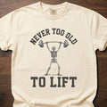 Never Too Old gym lifestyle shirt featuring skeleton lifting barbell overhead – Ivory